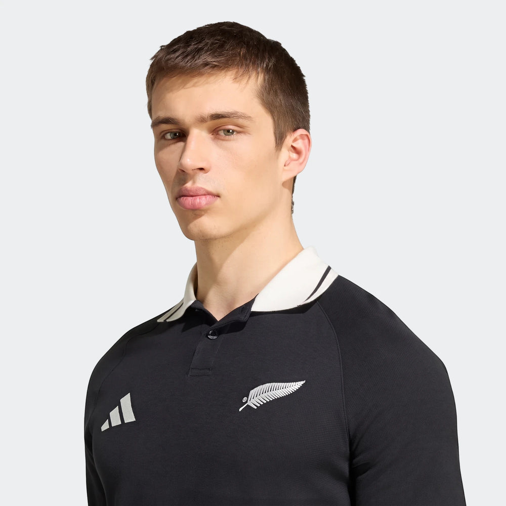 Close-up of a male model wearing a black New Zealand Rugby Leisurewear Polo Shirt with a white collar and raglan sleeves.