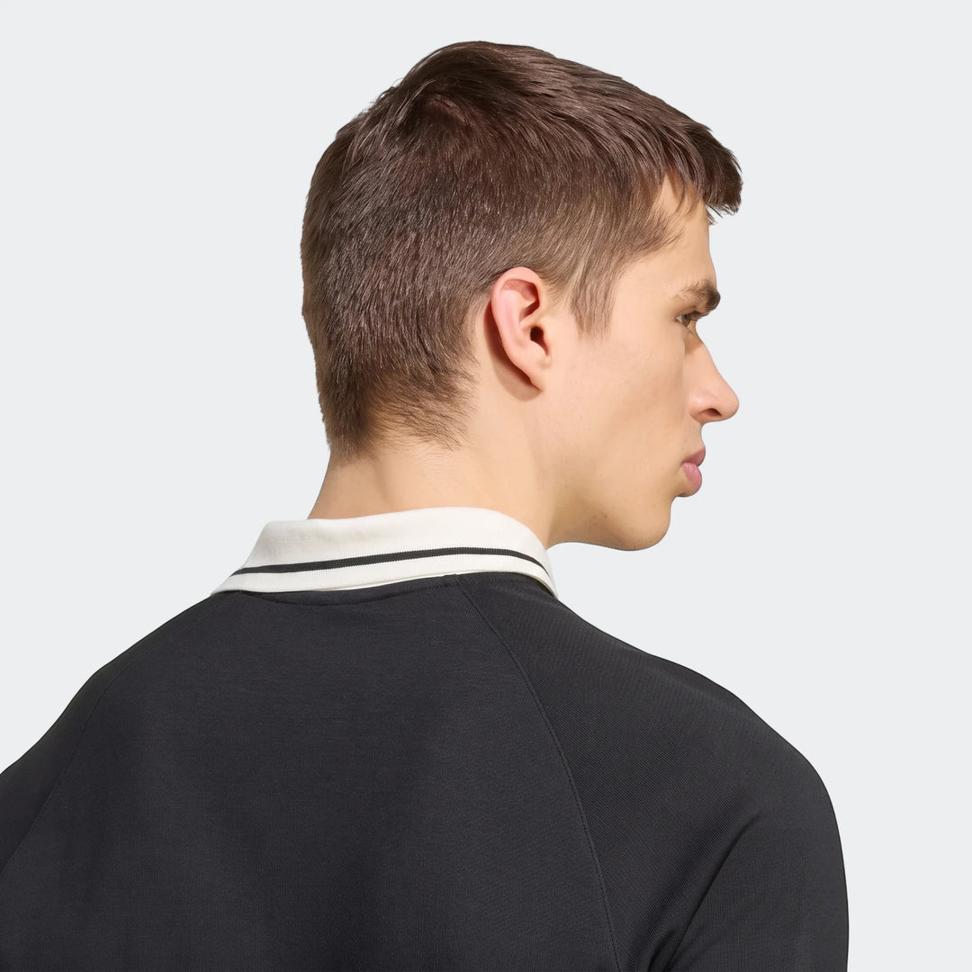 Male model wearing a black New Zealand Rugby Leisurewear Polo Shirt with a white striped collar, viewed from the side.