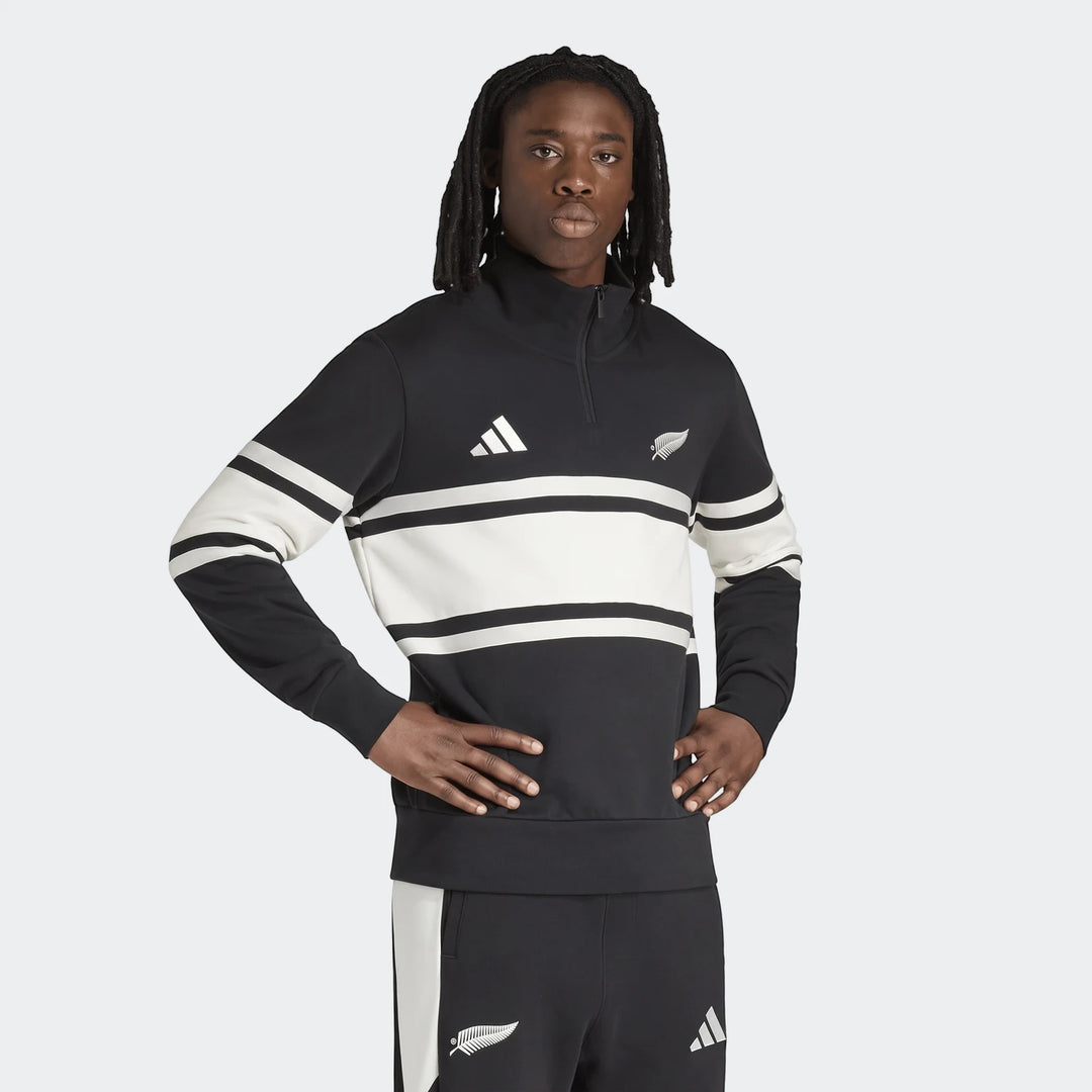 A male model wears the black and white New Zealand Rugby Leisurewear Quarter Zip Sweatshirt, featuring iconic stripes and