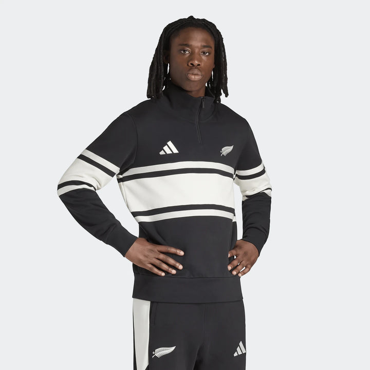 A male model wears the black and white New Zealand Rugby Leisurewear Quarter Zip Sweatshirt, featuring iconic stripes and