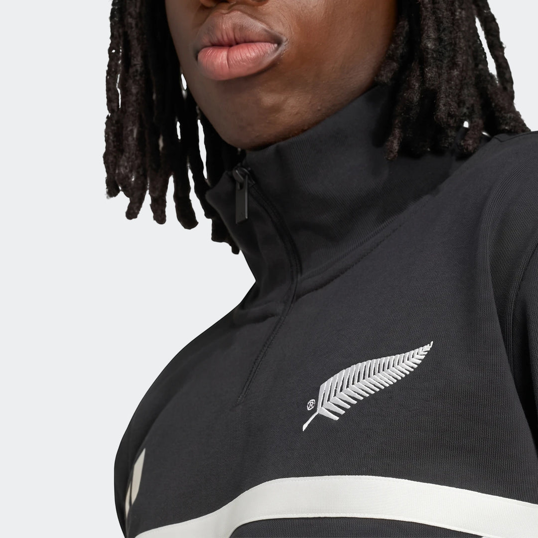 Close-up of a black New Zealand Rugby Leisurewear Quarter Zip Sweatshirt with a silver fern logo and white stripe, worn by a