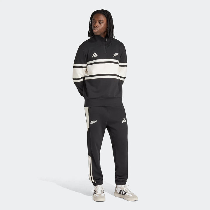 Male model wearing a New Zealand Rugby Leisurewear Quarter Zip Sweatshirt and track pants in black and white, standing in a