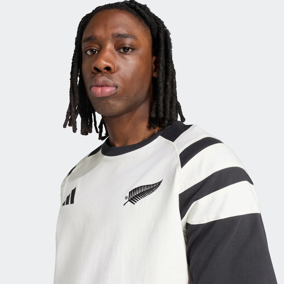 A young man wearing a white and black New Zealand Rugby Leisurewear T-Shirt with shoulder stripes and a fern logo.