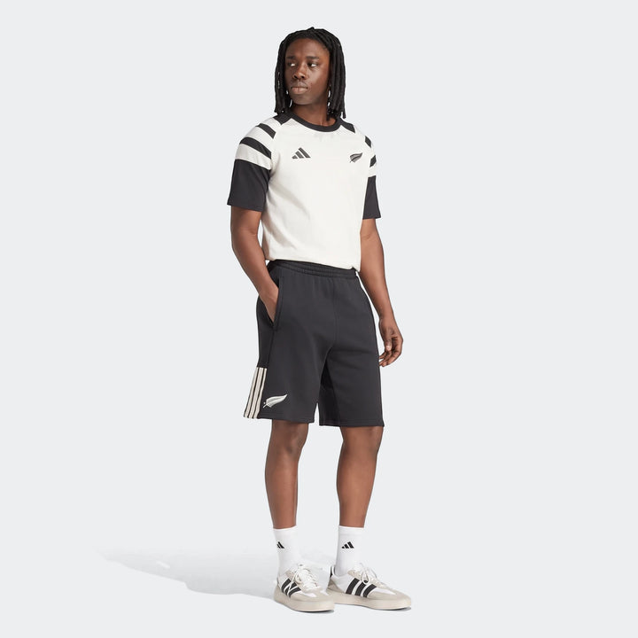 A male model wearing a New Zealand Rugby Leisurewear T-shirt and black shorts, featuring Adidas and fern logos, in a full