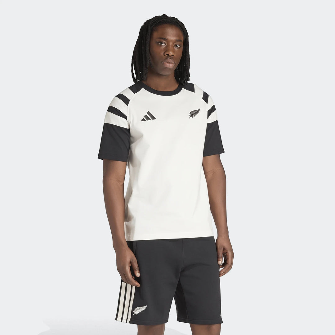 Male model wearing an off-white and black Adidas New Zealand Rugby Leisurewear T-shirt and black shorts, standing front view.
