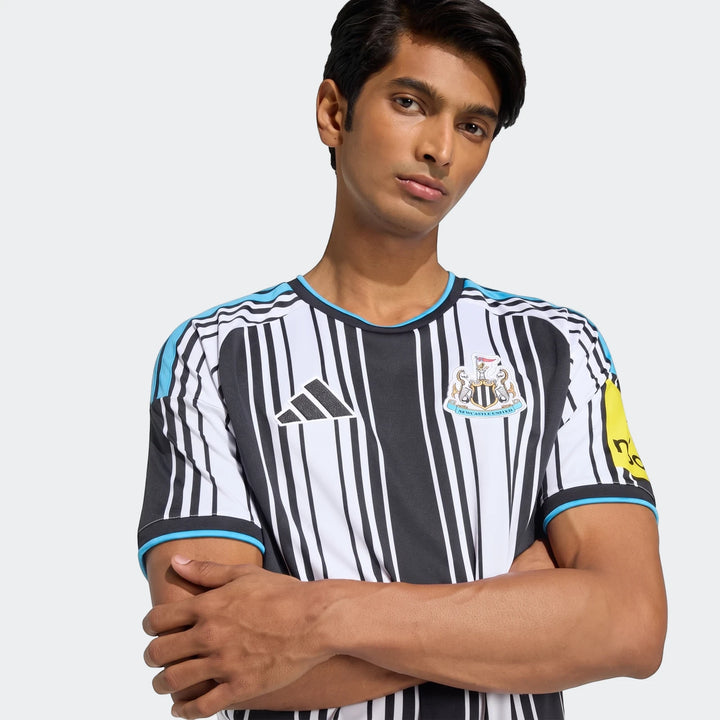 Male model in a black and white striped Newcastle United FC 26/27 home jersey with blue details, featuring club crest and