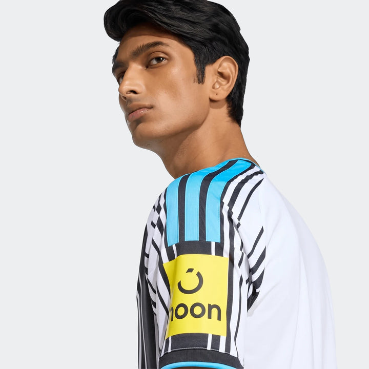 Close-up of a man wearing the Newcastle United Fc 26/27 Home Jersey, featuring black and white stripes, blue accents, and a