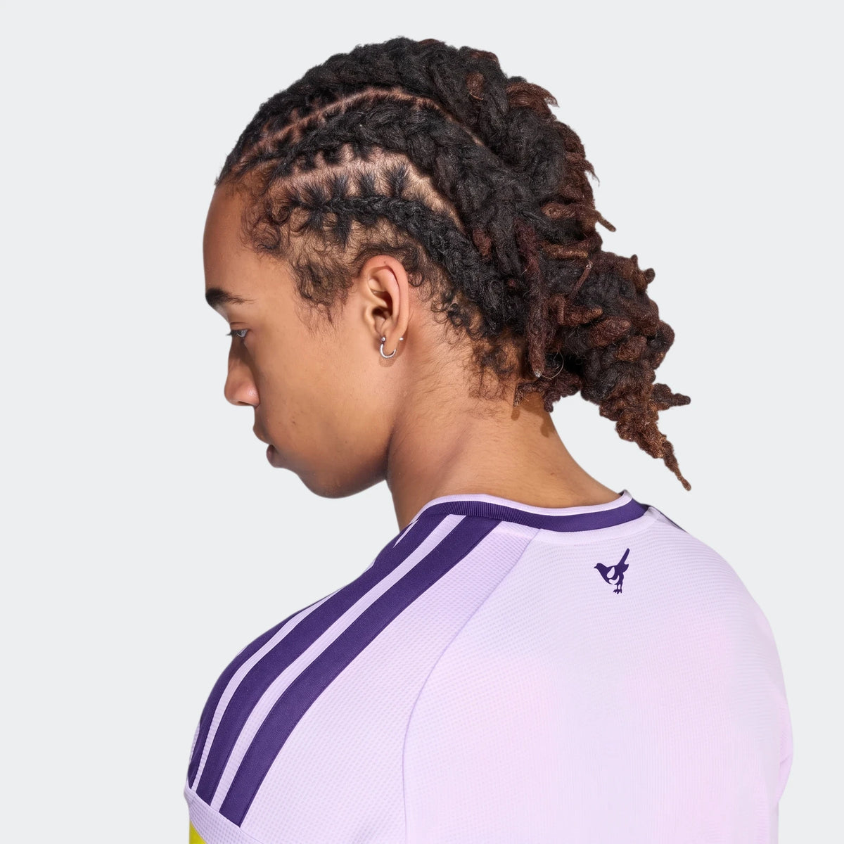 Close-up back-left view of a person with dreadlocks wearing a light purple Newcastle United FC 26/27 Third Jersey with dark