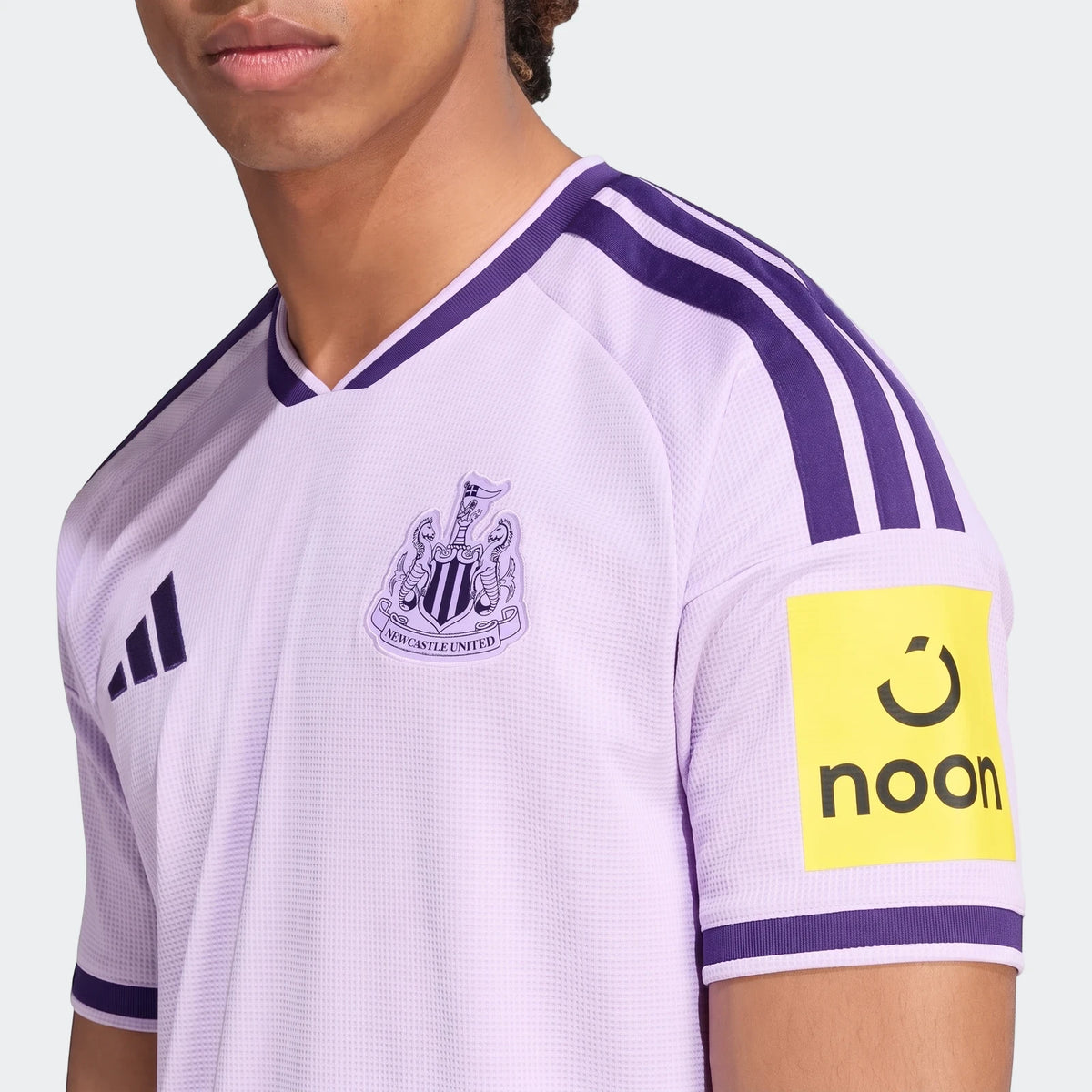 Close-up of a person wearing the Newcastle United Fc 26/27 Third Jersey in lilac with purple stripes and sponsor logo.