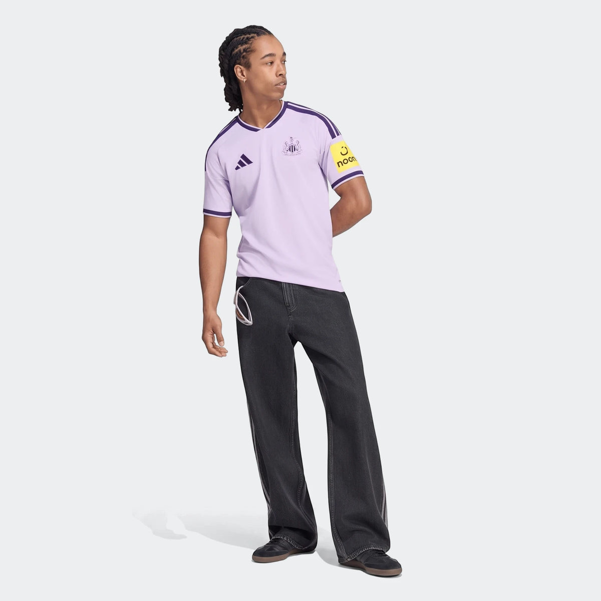 Male model wearing a light purple Newcastle United Fc 26/27 Third Jersey and dark gray jeans, full body on a white