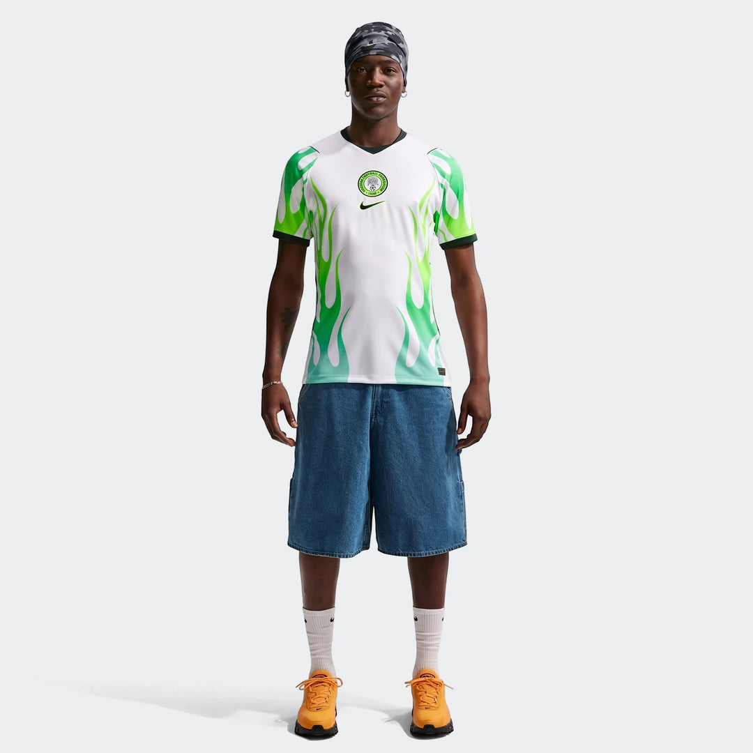 Male model wearing a Nigeria 2026 Stadium Away Men's Nike Dri-Fit Soccer Replica Jersey with green flame design, blue denim