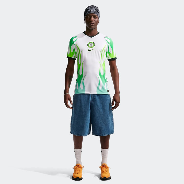 Male model wearing a Nigeria 2026 Stadium Away Men's Nike Dri-Fit Soccer Replica Jersey with green flame design, blue denim