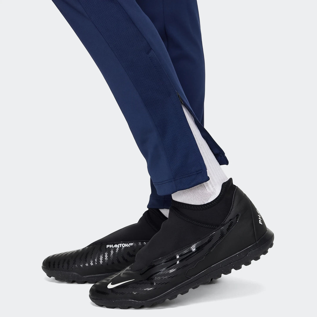 Close-up of a person wearing blue Nike Academy Big Kids' Dri-Fit Soccer Pants with black Nike Phantom cleats and white socks.