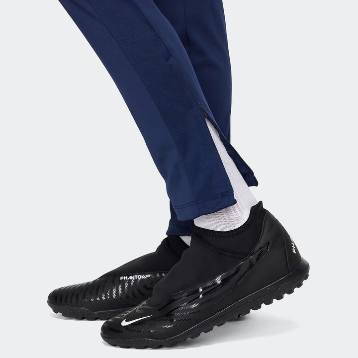 Close-up of a person wearing blue Nike Academy Big Kids' Dri-Fit Soccer Pants with black Nike Phantom cleats and white socks.