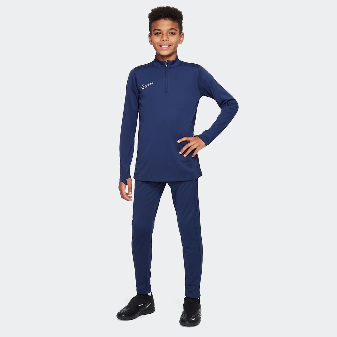Young boy in navy blue Nike Academy Big Kids' Dri-Fit soccer pants and matching quarter-zip top, full body shot.