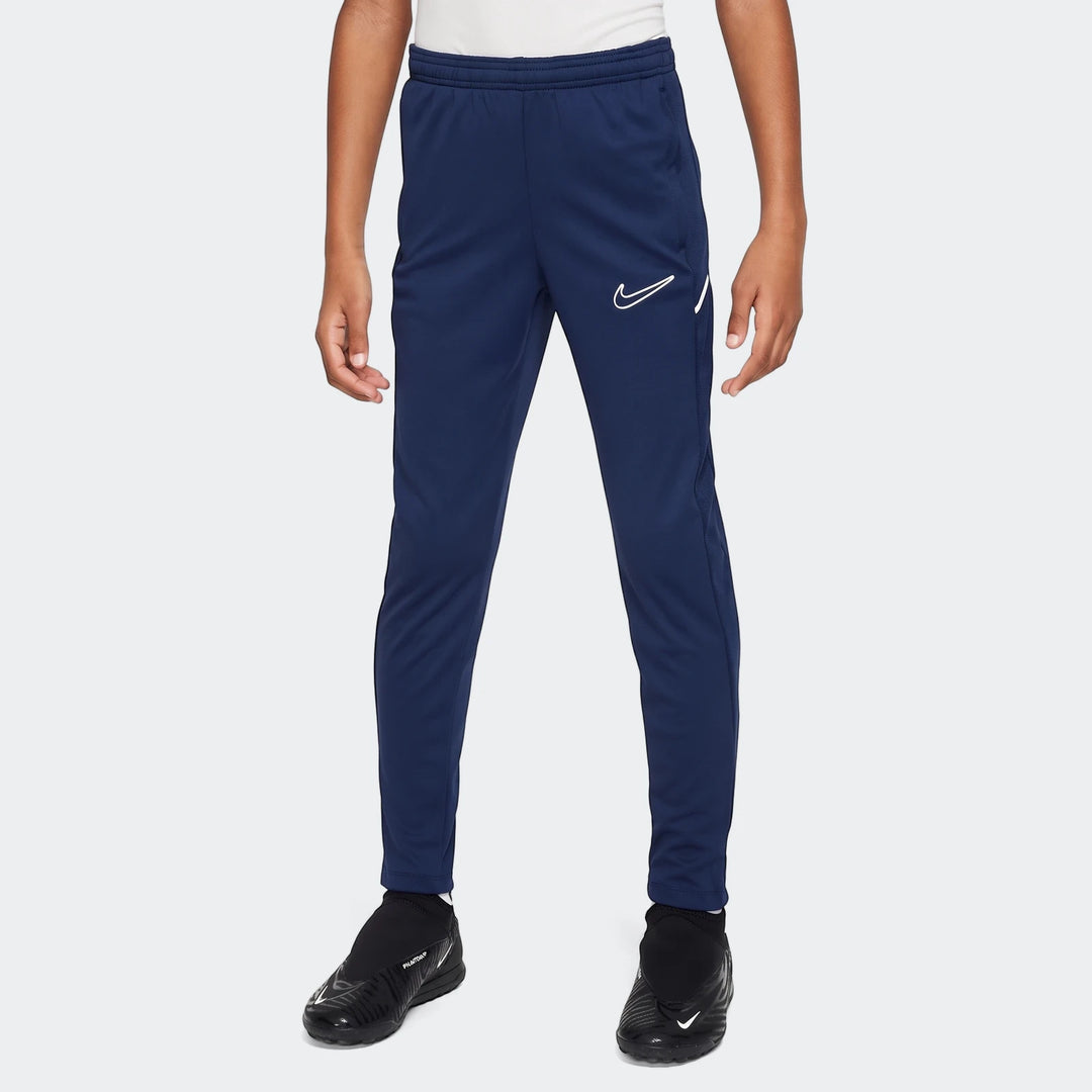 Dark blue Nike Academy Big Kids' Dri-Fit soccer pants, shown on a person from mid-torso to ankle, with black shoes.