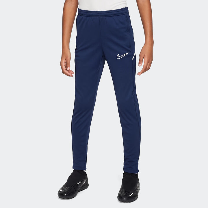 Dark blue Nike Academy Big Kids' Dri-Fit soccer pants, shown on a person from mid-torso to ankle, with black shoes.