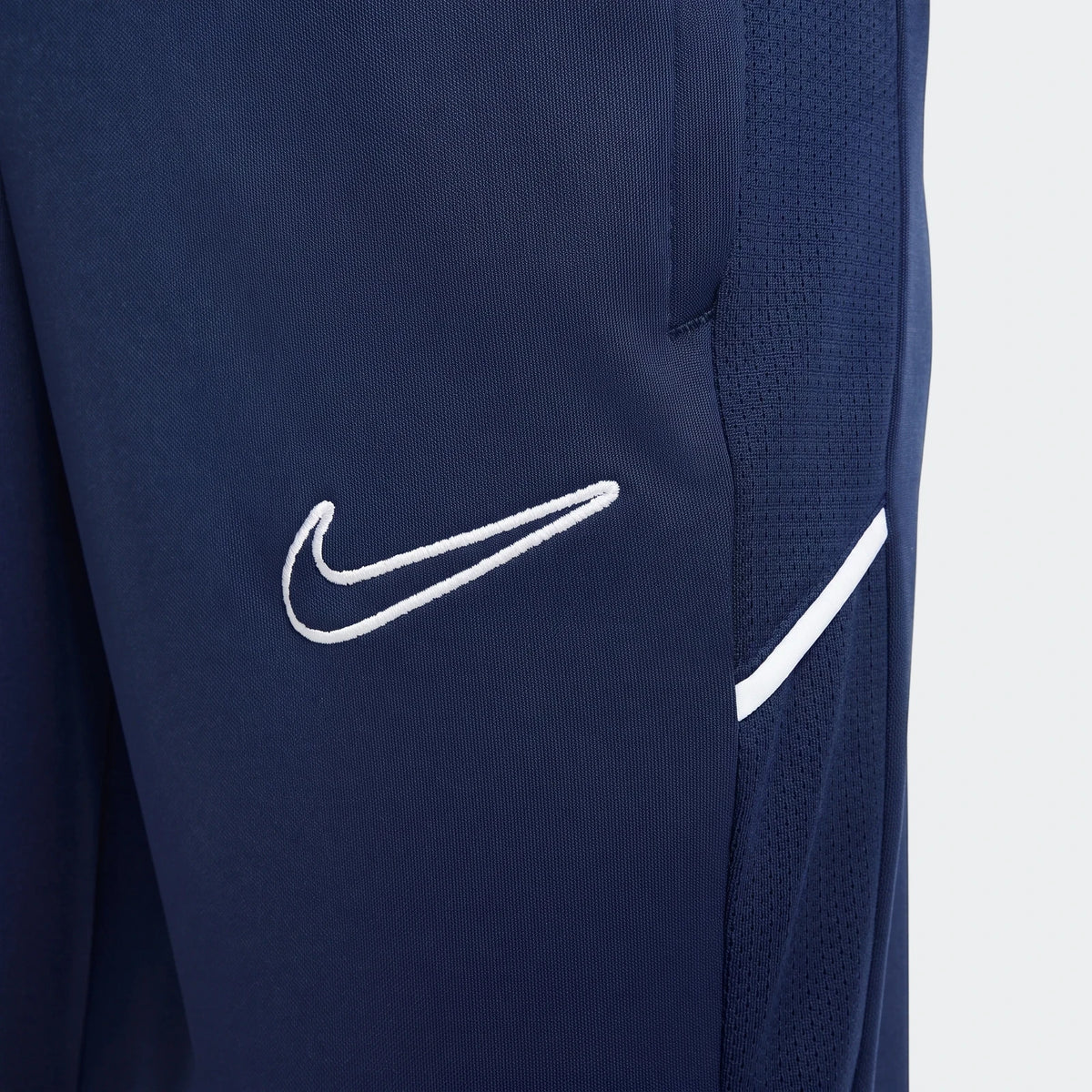 Close-up of Nike Academy Big Kids' Dri-Fit soccer pants in dark blue, featuring a white Nike swoosh logo and side stripe on