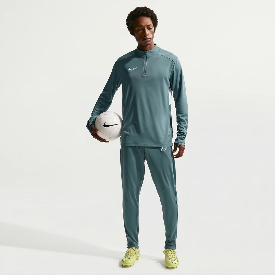 Full body shot of a man wearing a Nike Academy green long-sleeve Dri-Fit soccer drill top, matching pants, and neon cleats,