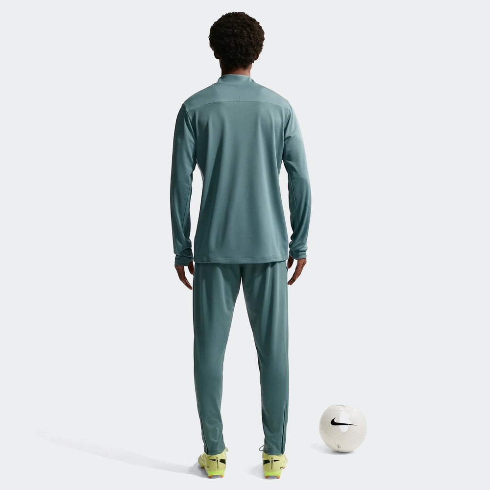 Full body back view of a man wearing Nike Academy green Dri-Fit soccer pants and matching long-sleeve top, standing with a