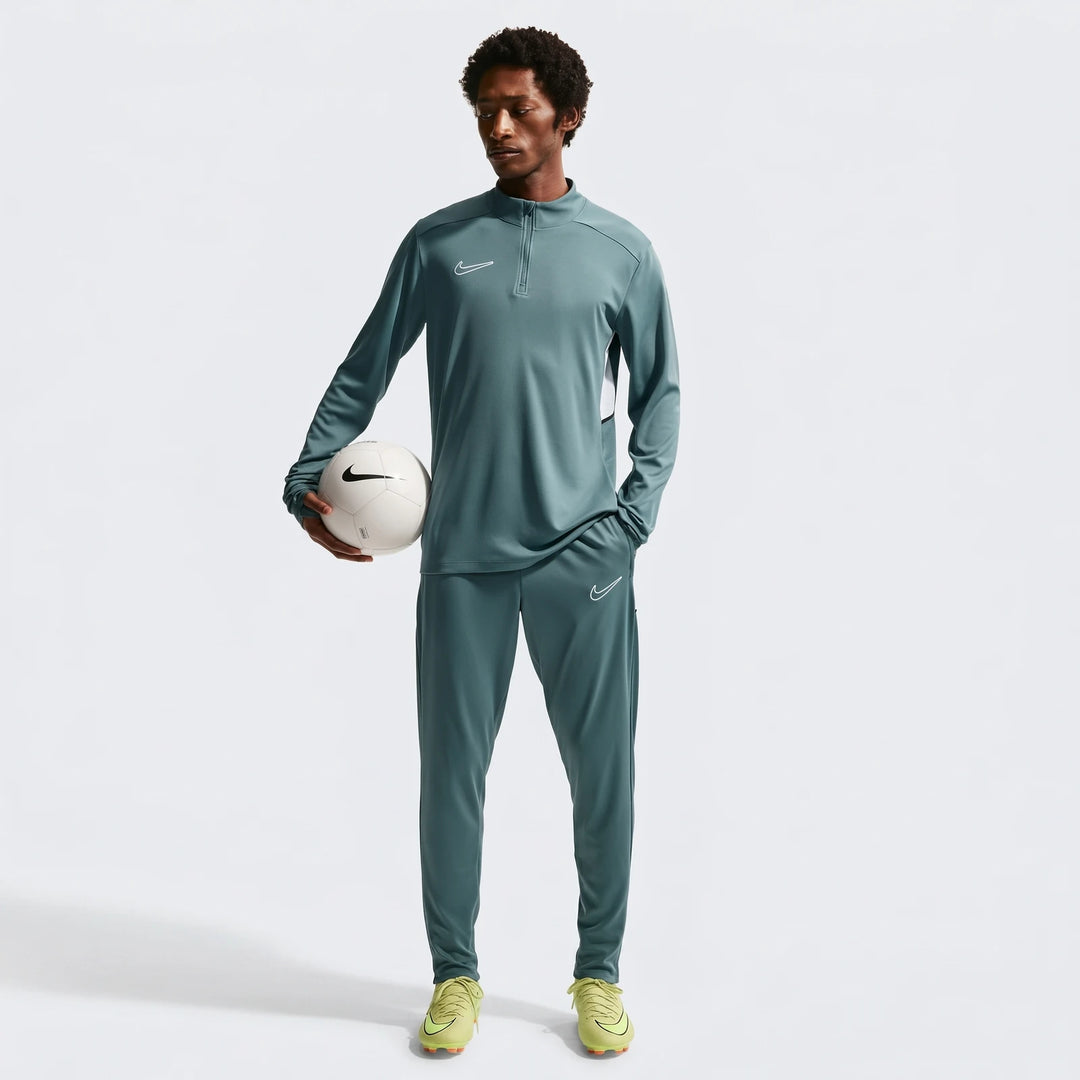 Male model in a full Nike Academy green Dri-Fit soccer tracksuit with neon yellow cleats, holding a white soccer ball,