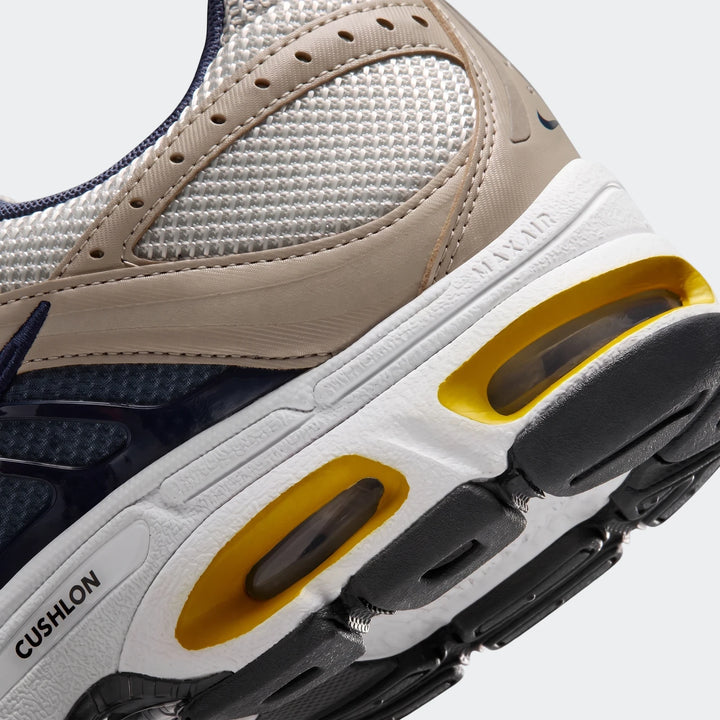 Close-up of a Nike Air Max Moto 2K 2Tone men's shoe, showcasing the navy, beige, white, and yellow colors with visible Max