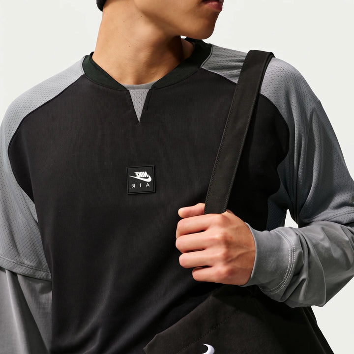Close-up of a man wearing a black and grey Nike Air long-sleeve top with mesh panels and a white logo patch.