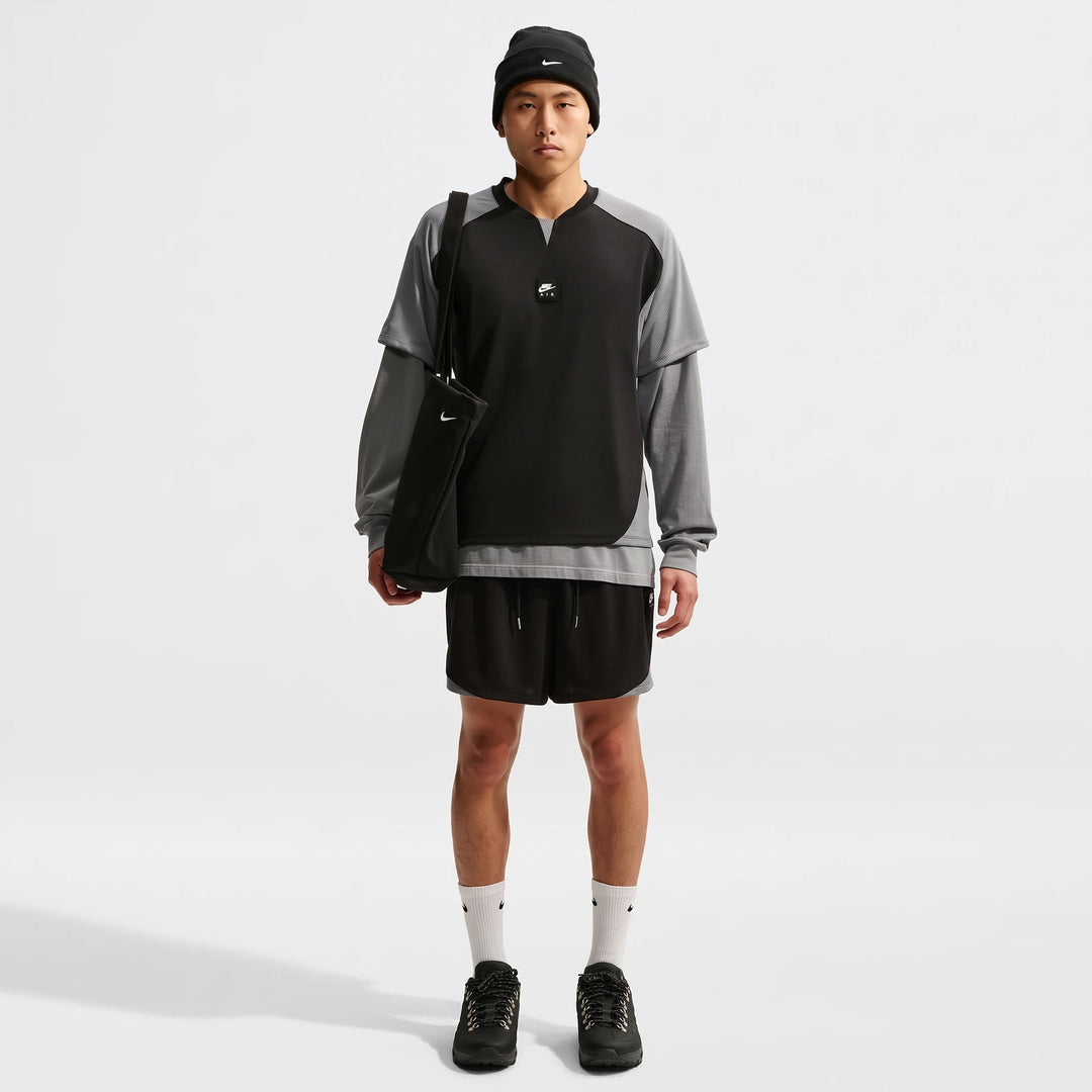Man wearing a black and grey Nike Air Men's Top, black shorts, beanie, and holding a black tote bag, full body shot.