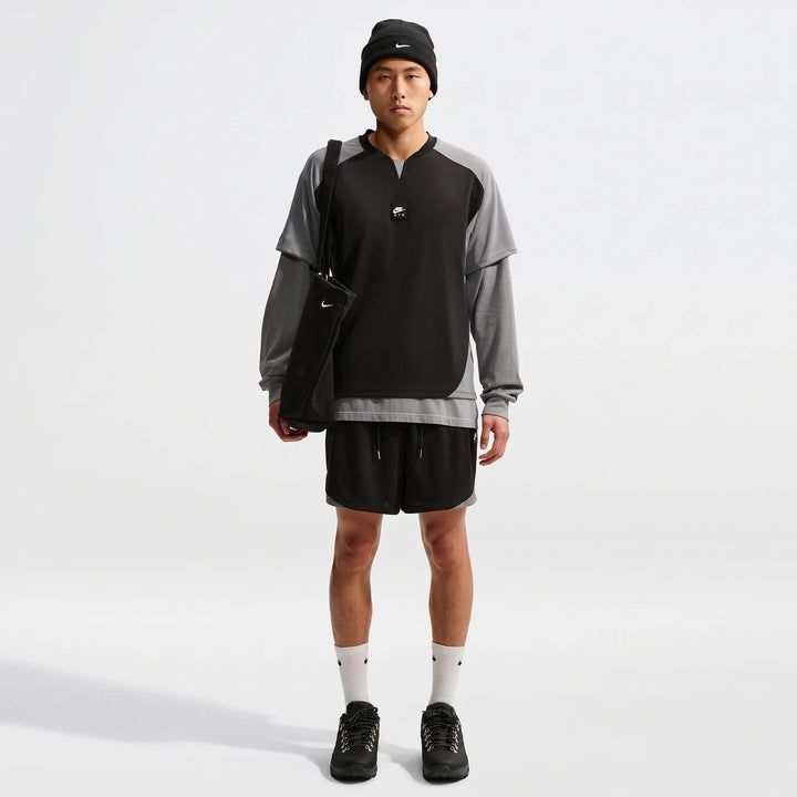 Man wearing a black and grey Nike Air Men's Top, black shorts, beanie, and holding a black tote bag, full body shot.