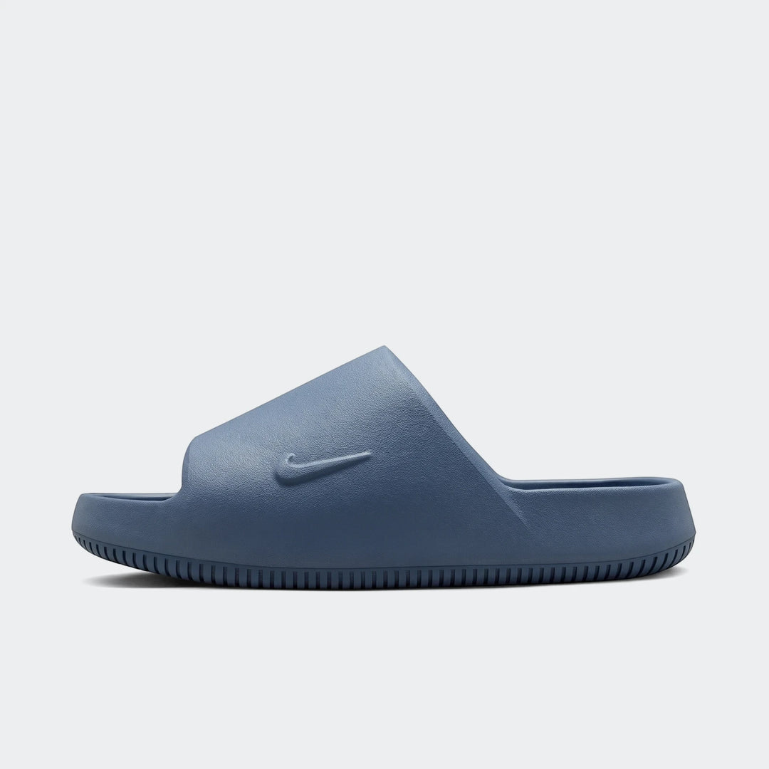 Side profile of a single Nike Calm 2.0 Men's Slide in a deep blue color, featuring a textured surface and embossed swoosh