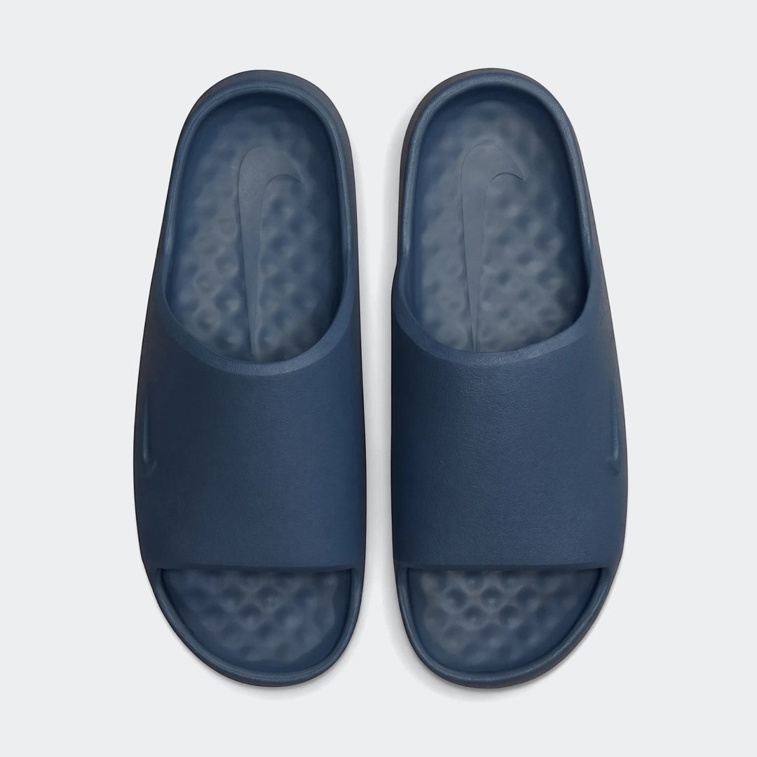 Overhead view of a pair of deep blue Nike Calm 2.0 Men's Slides with textured footbeds and debossed swoosh logos.