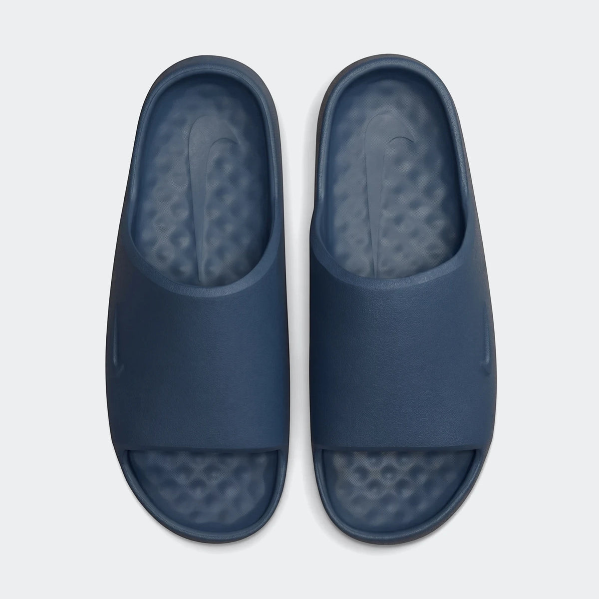 Overhead view of a pair of deep blue Nike Calm 2.0 Men's Slides with textured footbeds and debossed swoosh logos.