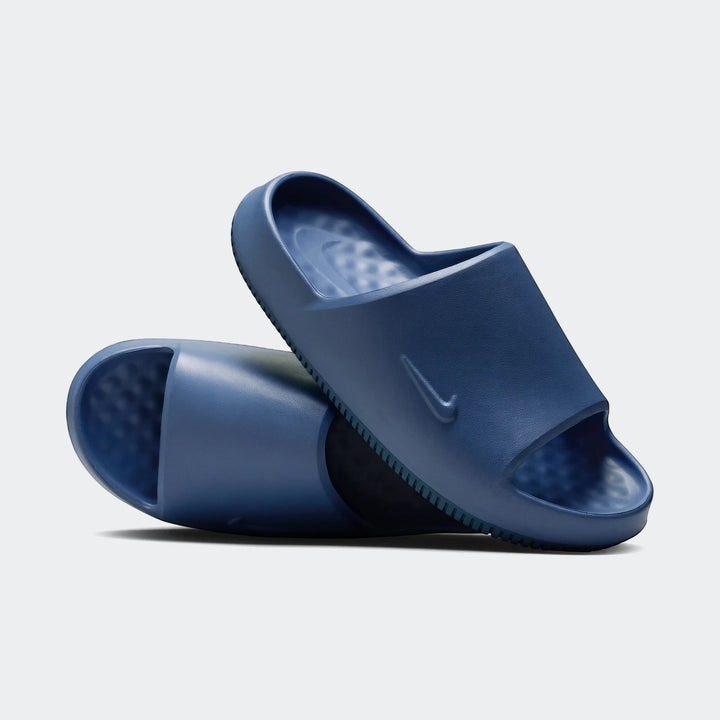 A pair of blue Nike Calm 2.0 men's slides, one upright and one angled behind, showcasing their smooth molded design and