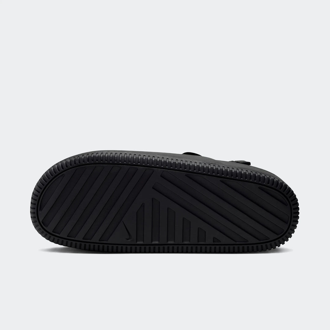 Bottom view of a black Nike Calm men's mule, showcasing the textured sole with a distinct tread pattern and Nike swoosh logo.