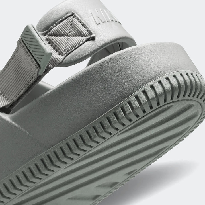 Close-up view of a single grey Nike Calm Men's Mule sandal, showing the textured sole, rubber body, and woven strap detail.