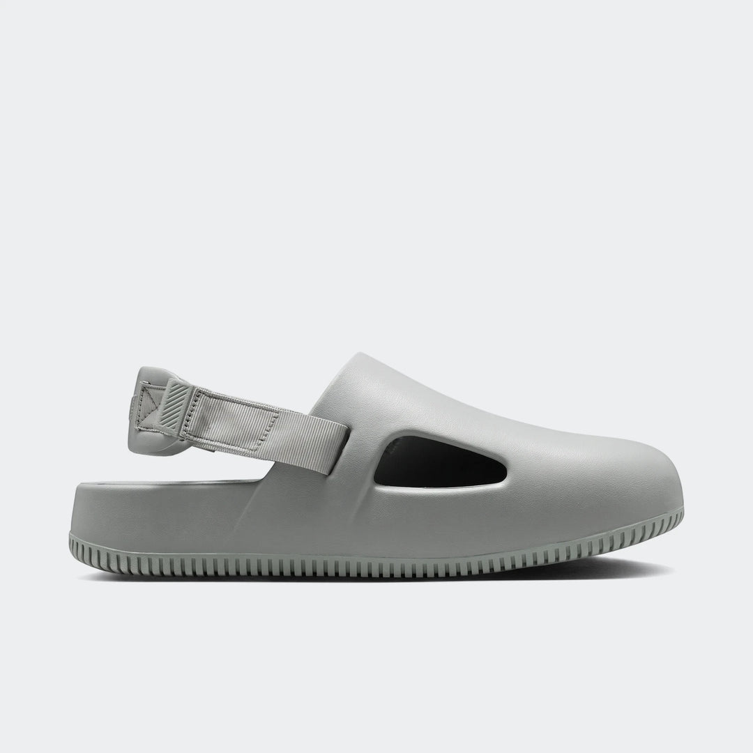 A light grey Nike Calm Men's Mule, made of comfortable foam material, shown in a side profile view with a visible heel strap.
