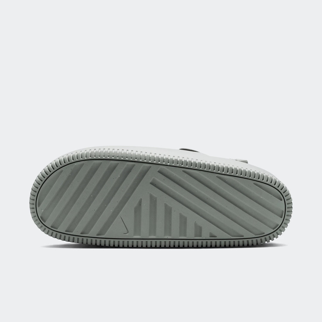 Nike Calm men's mules with a gray-green textured sole, featuring a Nike swoosh logo. Bottom view of the shoe.