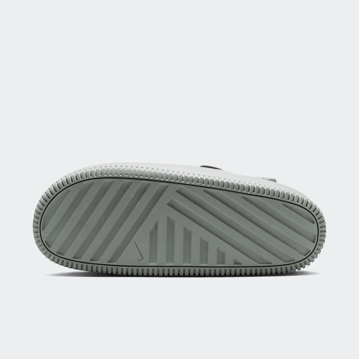 Nike Calm men's mules with a gray-green textured sole, featuring a Nike swoosh logo. Bottom view of the shoe.