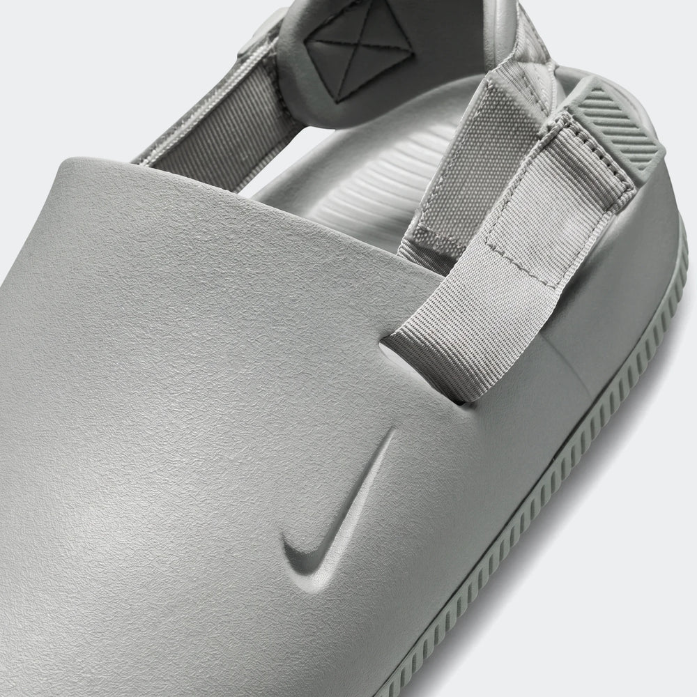 Close up of a grey textured Nike Calm Men's Mule sandal with woven straps and an embossed swoosh logo.