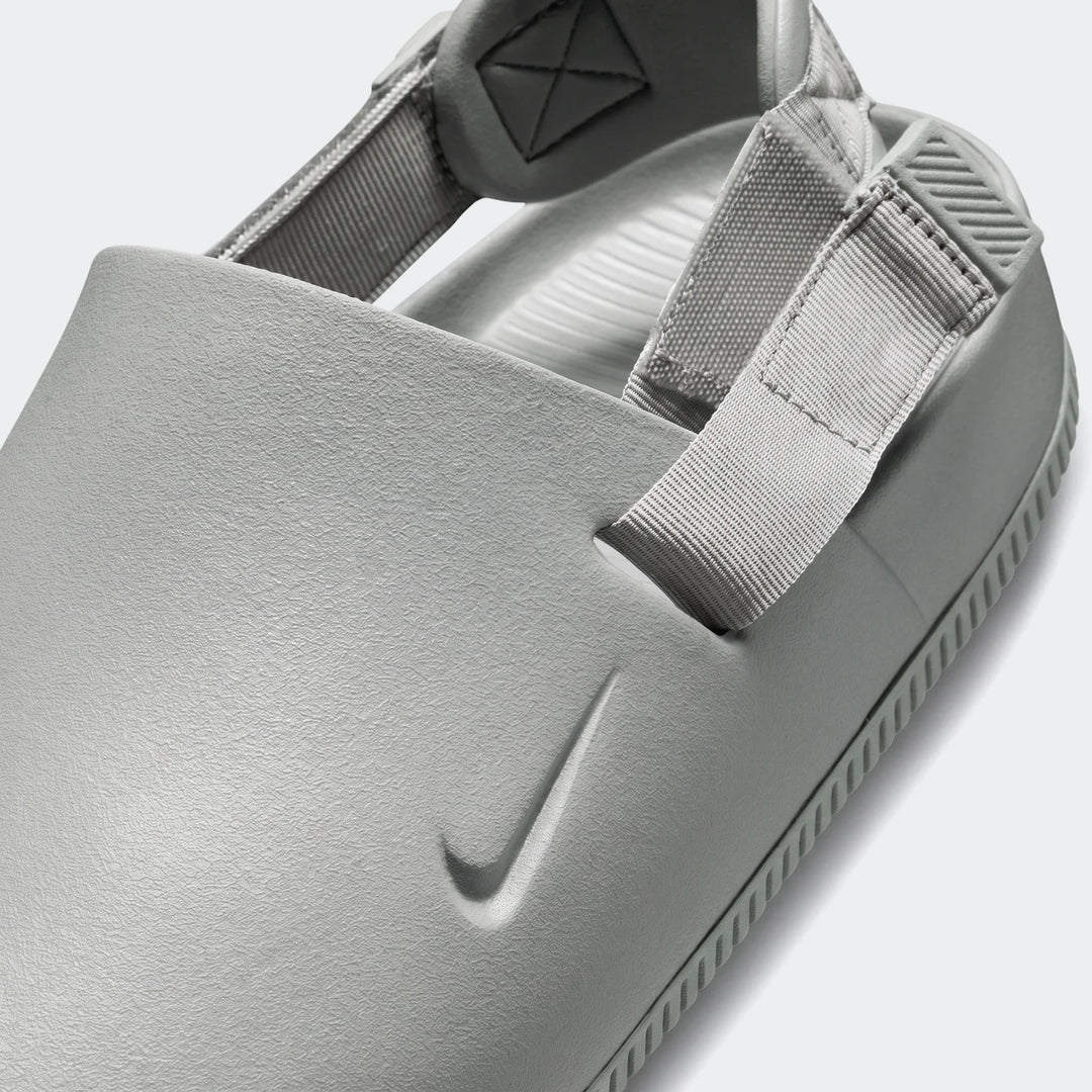 Close up of a grey textured Nike Calm Men's Mule sandal with woven straps and an embossed swoosh logo.