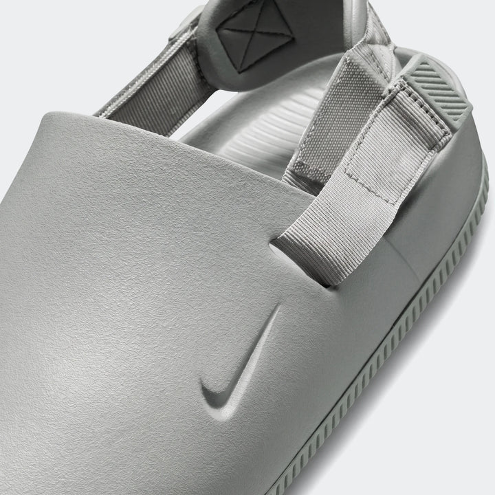 Close up of a grey textured Nike Calm Men's Mule sandal with woven straps and an embossed swoosh logo.