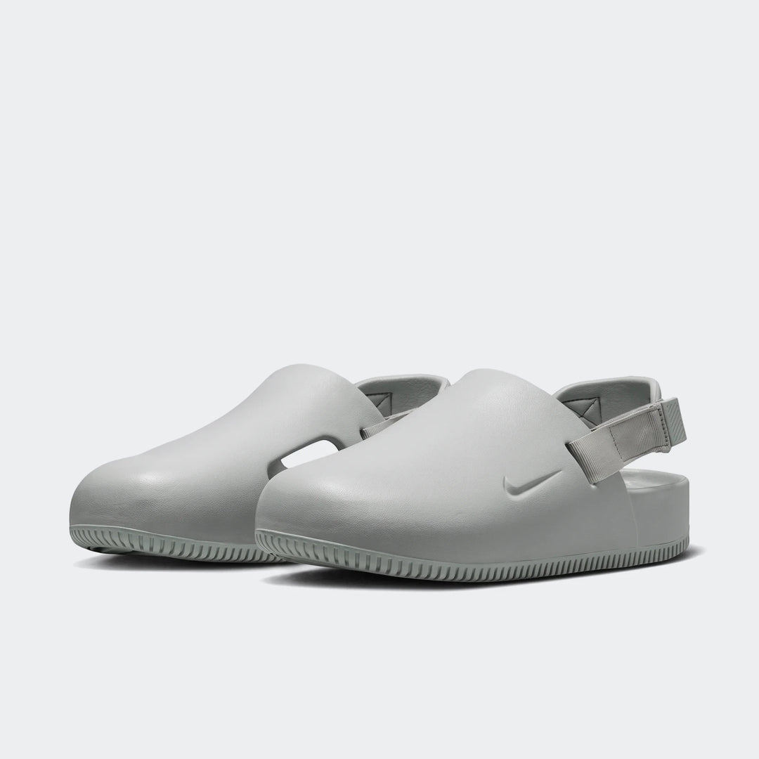 Pair of light gray Nike Calm Men's Mules, featuring a smooth molded design with a comfortable back strap and textured sole,