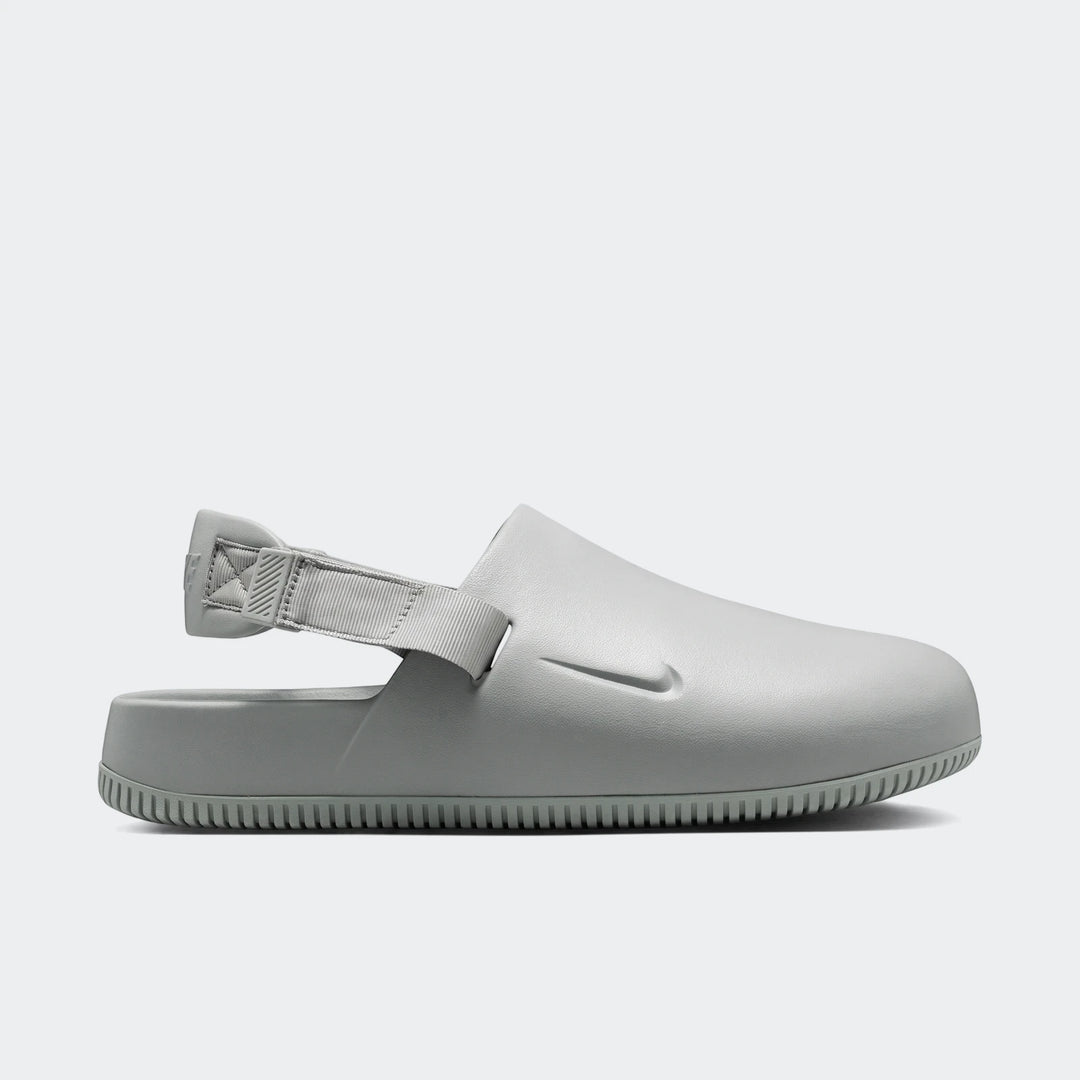 Light grey Nike Calm Men's Mules, shown in a side profile, featuring a smooth slip-on design with an adjustable heel strap.