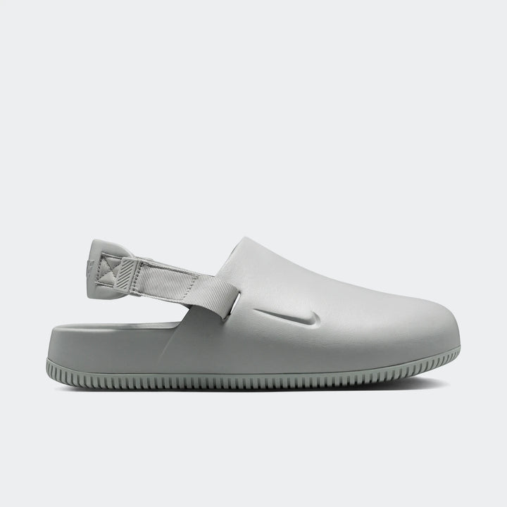 Light grey Nike Calm Men's Mules, shown in a side profile, featuring a smooth slip-on design with an adjustable heel strap.