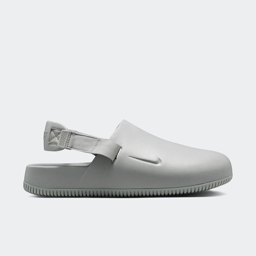 Light grey Nike Calm Men's Mules, shown in a side profile, featuring a smooth slip-on design with an adjustable heel strap.