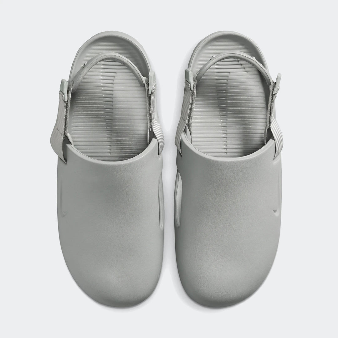 A pair of light grey Nike Calm men's mules, featuring adjustable straps and a ribbed footbed, presented in a top-down view.