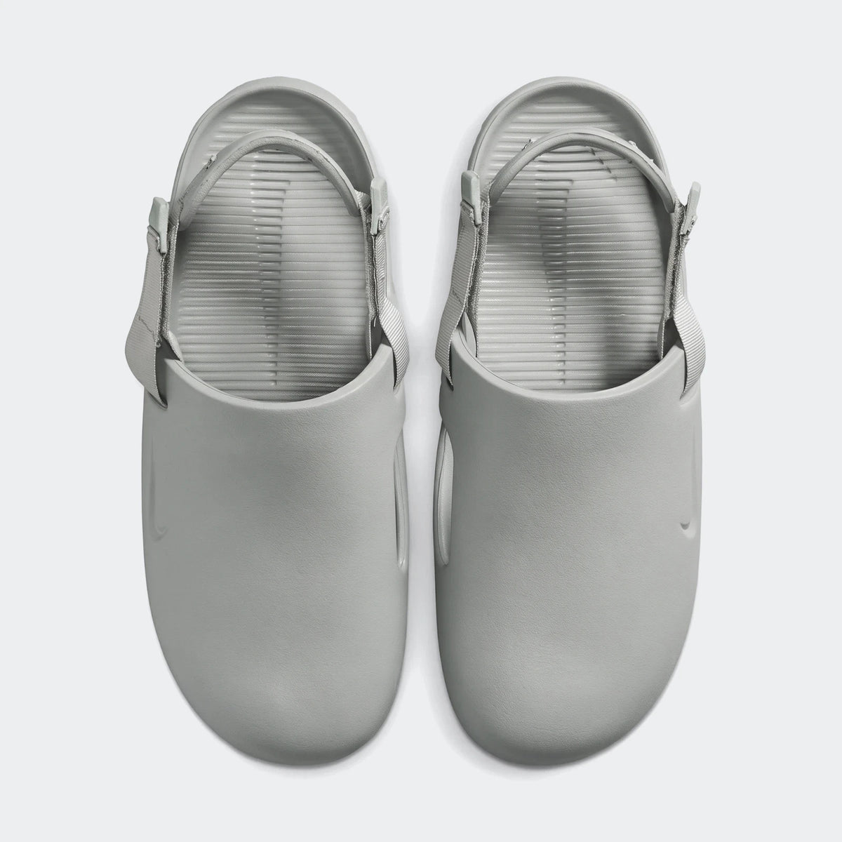A pair of light grey Nike Calm men's mules, featuring adjustable straps and a ribbed footbed, presented in a top-down view.
