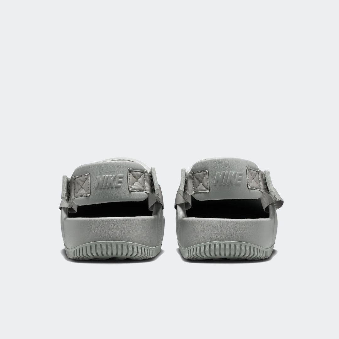Rear view of two Nike Calm Men's Mules in a muted sage green, featuring molded foam construction, ribbed soles, and embossed