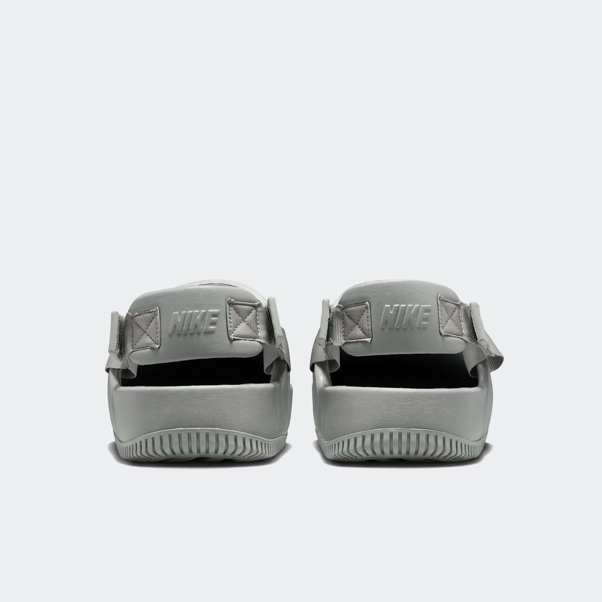 Rear view of two Nike Calm Men's Mules in a muted sage green, featuring molded foam construction, ribbed soles, and embossed