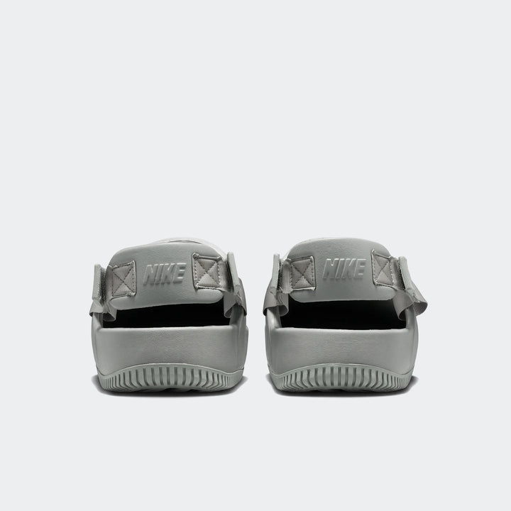 Rear view of two Nike Calm Men's Mules in a muted sage green, featuring molded foam construction, ribbed soles, and embossed